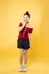 Smiling young woman poses in a red off the shoulder top against a solid yellow background