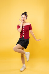 Cheerful woman in red top and shorts strikes a playful pose against a vibrant yellow backdrop