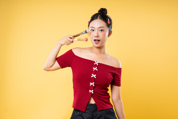 Woman with makeup brushes near her face against a yellow background showcasing beauty and fun