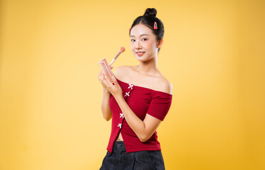 Young woman with makeup palette and brush on yellow background doing her makeup routine
