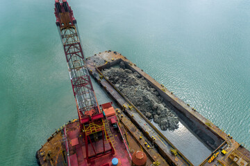 Crane barge transferring excavated rocks and sediment into a nearby container vessel during...