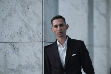 Handsome confident businessman in suit stands against stone wall.