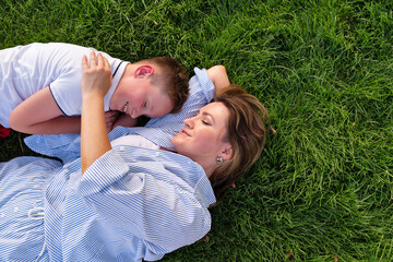From above, a grinning boy nestles against his mother as they lounge on bright grass, enjoying...