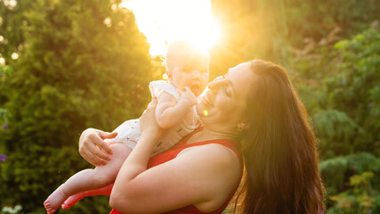 Mom tilts her laughing baby toward the blazing sunburst, both framed by soft green foliage and...