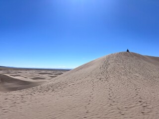 A hiker perched on a great sand dune in the desert 