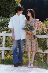 Young couple in a garden holding flowers surrounded by nature.