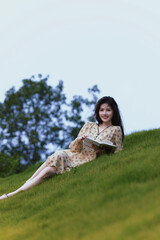 A young woman reading a book while relaxing on a grassy hill.