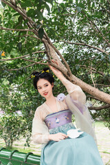 Young woman in traditional attire sitting on a bench under a tree Chinese word means flower.