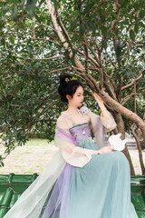 Woman in traditional attire sitting among trees with a serene expression.