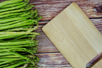 Bunch of fresh green asparagus stems with cutting wooden board on wooden background