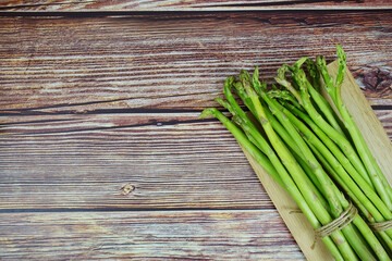 Bunch of fresh green asparagus stems with cutting wooden board on wooden background