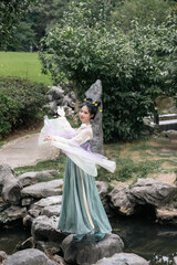 Woman in flowing dress gracefully twirls near a rocky stream surrounded by greenery Chinese word...