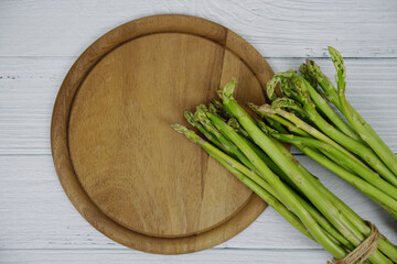 Bunch of fresh green asparagus stems with cutting wooden board on wooden background