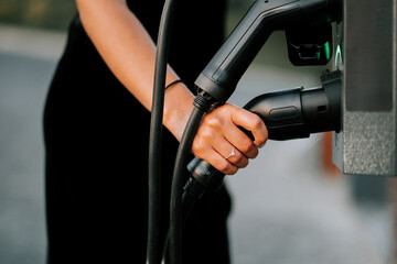Person charging an electric vehicle at a charging station in the evening light
