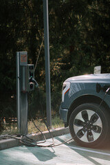 Electric vehicle charging station seen in a green outdoor area with a parked car