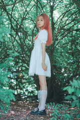 Young woman in a white dress standing in a lush green setting.