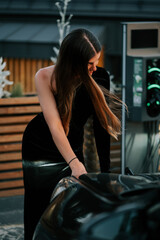 Elegant woman interacts with luxury car at urban charging station during evening