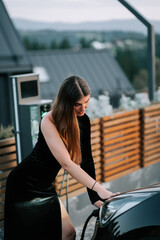 Woman in elegant black dress charging electric vehicle in scenic outdoor setting