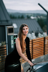 Model poses elegantly beside a sleek car on a rooftop at dusk with a stunning view