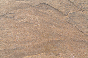 Abstract shapes and patterns in grainy sand and flowing water on the beach on a sunny day, viewed from above. Abstract textured natural sandy background, top view. Copy space.