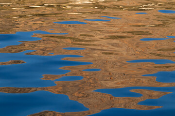 Abstract blue and brown reflections on rippled water surface. Background with abstract natural shapes and vibrant colors.