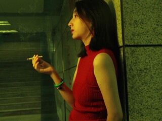 Profile of a young woman smoking in a dimly lit setting.