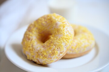 Two summer-inspired glazed donuts with yellow sugar topping on a white plate. Bright and cheerful, perfect for a seasonal café menu or dessert promotion.