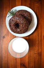 Chocolate donuts with crunchy topping served with a glass of milk on a wooden table. Perfect for cafes, restaurant menus, bakeries, and food promotions. Warm, indulgent, and inviting.