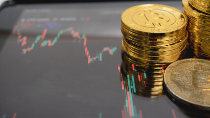 Stack of gold colored Bitcoin coins is placed digital tablet displaying financial chart, symbolizing cryptocurrency trading and investment. image conveys sense of modern finance and digital