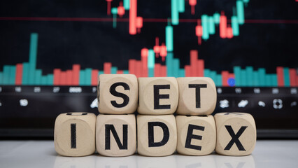 Stock market concept with wooden blocks spelling SET INDEX in front of financial chart displaying...