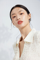 Portrait of a young woman with a stylish outfit and natural makeup against a light background.