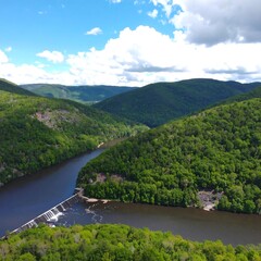 River bends through lush green mountains under a partly cloudy sky; a dam is visible
