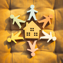 Wooden human figures around a house icon represent family, community, and homeownership. Ideal for...