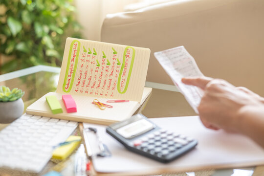 Parent is calculating school supply expenses using a calculator and a shopping list, preparing for back to school season and ensuring they have enough budget