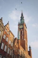 The historic Main Town Hall in Gdansk, Poland, with its intricate clock tower, stands tall against a pale blue sky. The image highlights the city's beautiful gothic architecture.