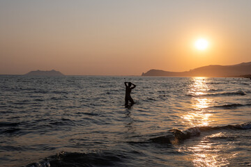 Silhouettes of swimming people on sunset in sun lights, sandy beach near Sperlonga, Lazio, italy,...