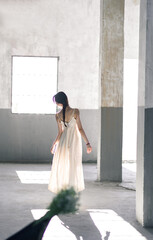A young woman in a simple dress walking in a sunlit industrial space.