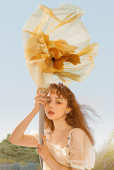 A young woman holding a large flower umbrella against a serene background.