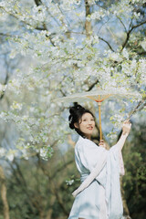 Woman in traditional attire holding a parasol among blooming trees Chinese word means blossom.