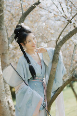 Young woman in traditional attire standing under blooming trees.