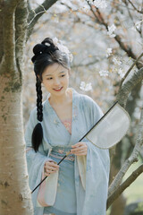 Young woman in traditional attire enjoying a sunny spring day under blossoming trees Chinese word...