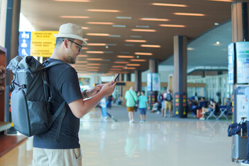 Back view of a young Asian man wearing backpack while looking at his smartphone.