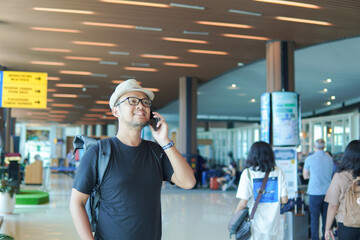 Smiling young Asian man using his smartphone to call while waiting at airport lounge lobby.