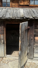Rustic village hut entrance featuring an aged wooden door ajar, allowing a glimpse into the...