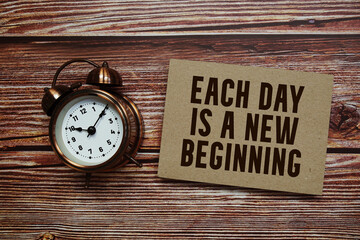 Each day is a new beginning text with alarm clock on wooden background