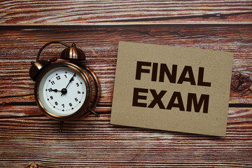 Final Exam text with alarm clock on wooden background