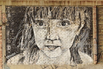 Detailed mural of a girl's face painted on a brick wall, showcasing intricate shading and expressive eyes.