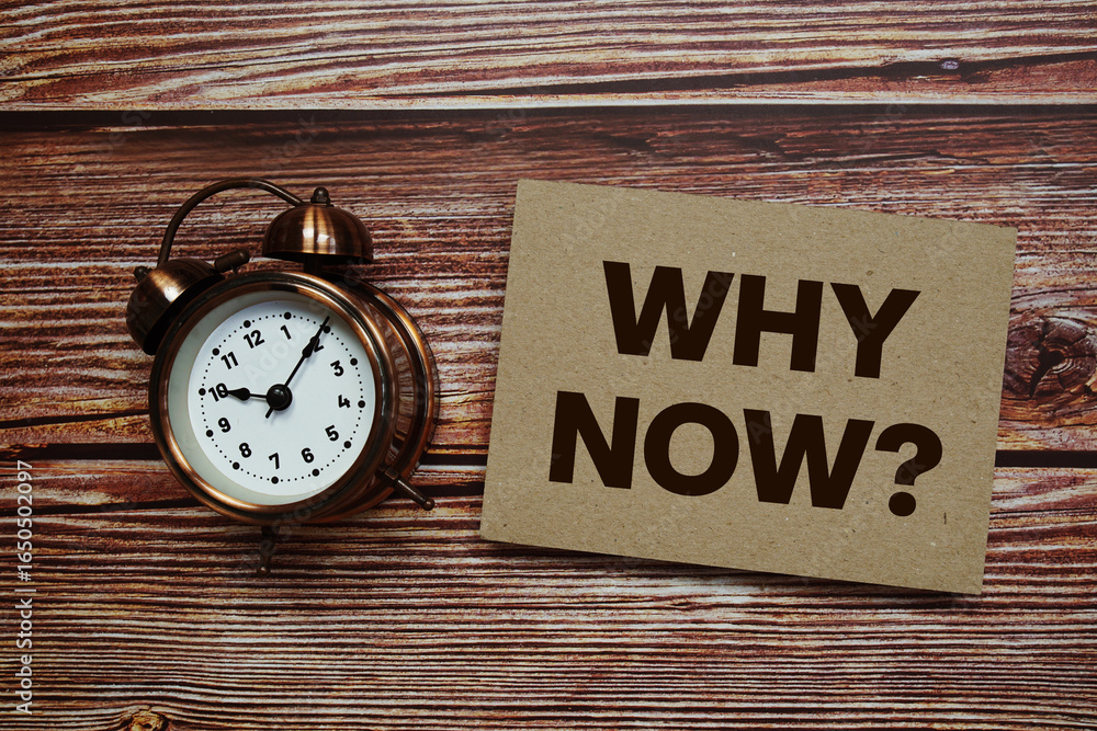 Poster why now? text with alarm clock on wooden background