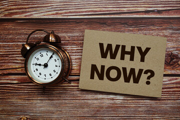 Why Now? text with alarm clock on wooden background