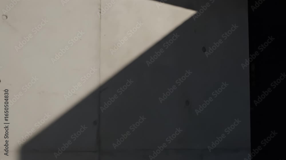 Poster a concrete wall is partially illuminated by sunlight casting a triangular shadow to the right is dar